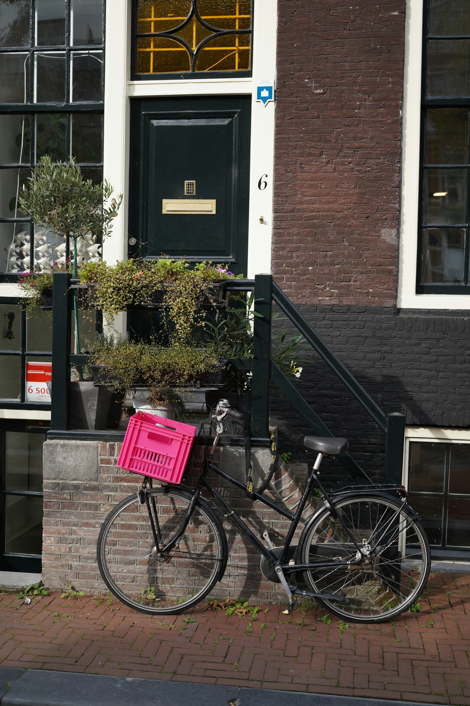 Een fiets met een krat staat voor de voordeur van een bakstenen huis.